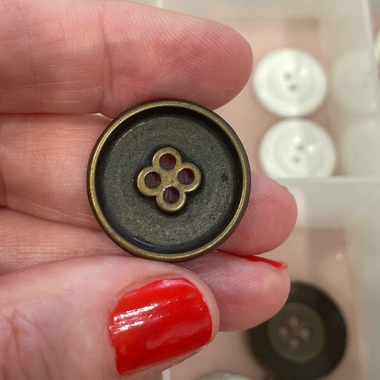 Hand holding a button with a clear container of buttons in the background