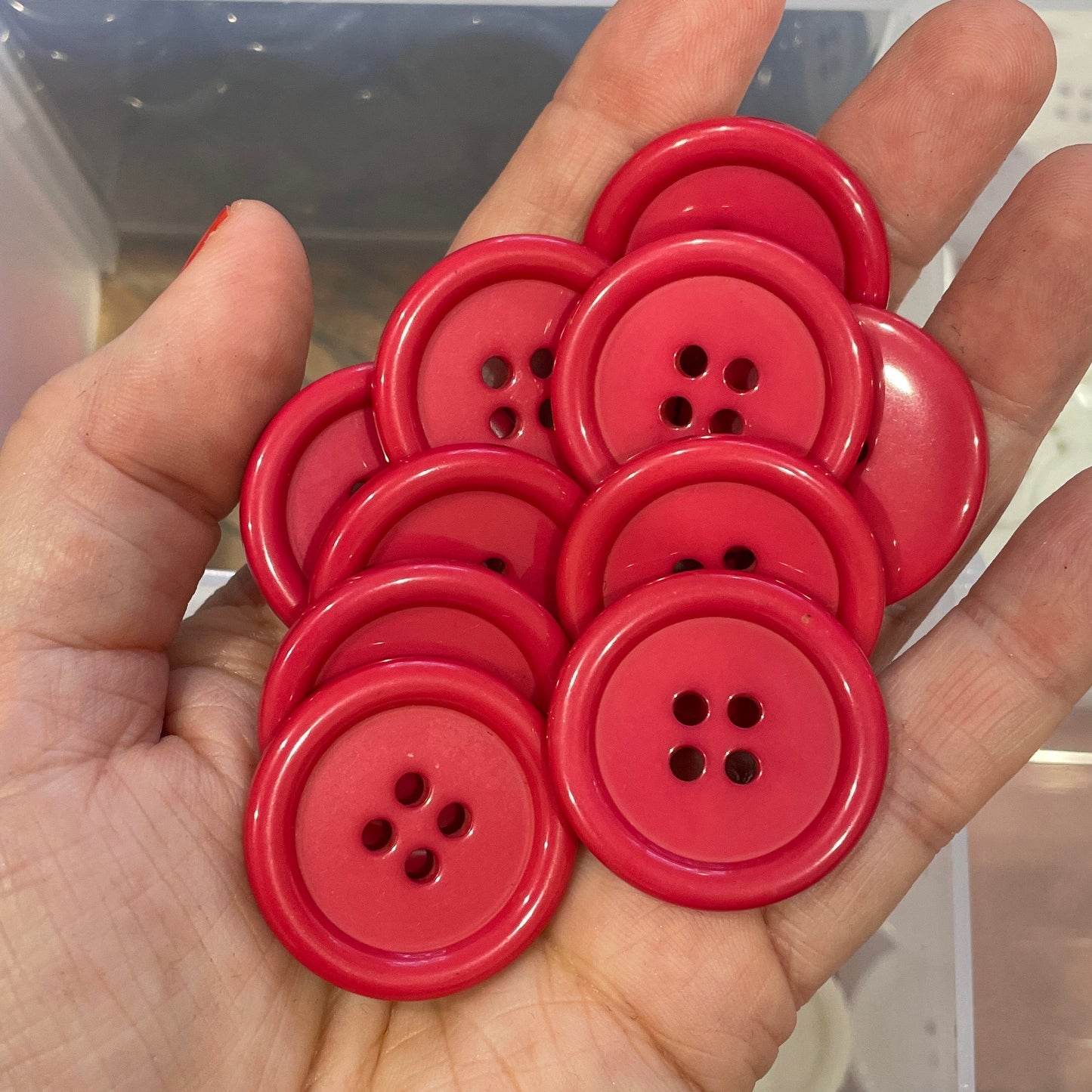 Hand holding red buttons with a background of black buttons in a clear container.