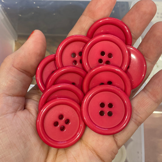 Hand holding red buttons with a background of black buttons in a clear container.