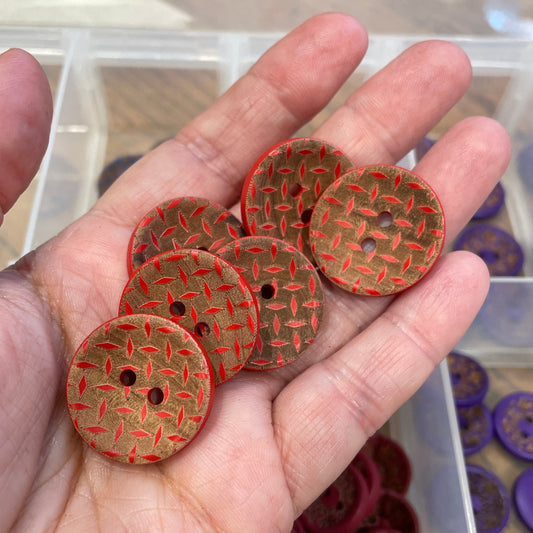 Hand holding red patterned buttons with a container of buttons in the background