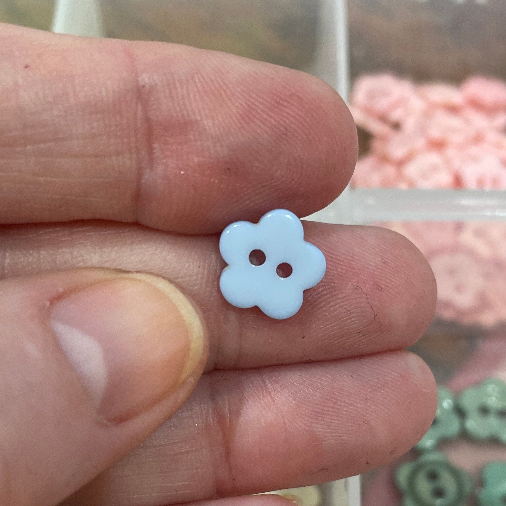 Hand holding a small white flower-shaped object with a clear container of colorful buttons in the background.
