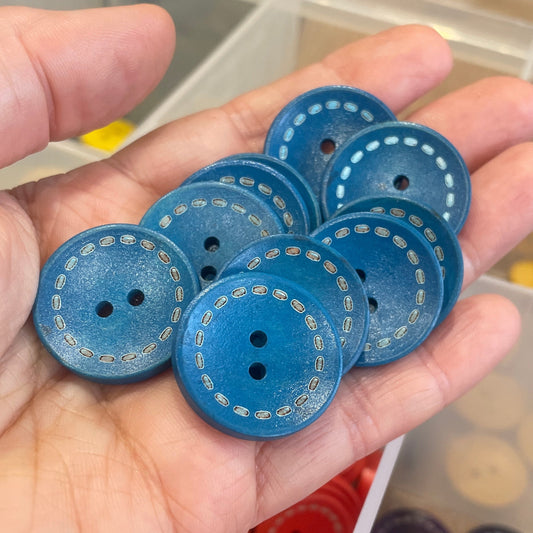 Hand holding blue buttons with a background of assorted buttons