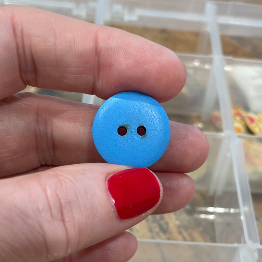 Hand holding a blue button with a clear container of buttons in the background
