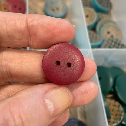Hand holding a red button with a container of buttons in the background