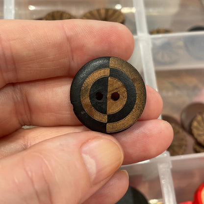 Hand holding a decorative button with a circular design, in front of a container filled with various buttons.