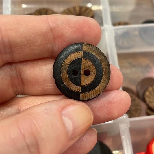 Hand holding a decorative button with a circular design, in front of a container filled with various buttons.