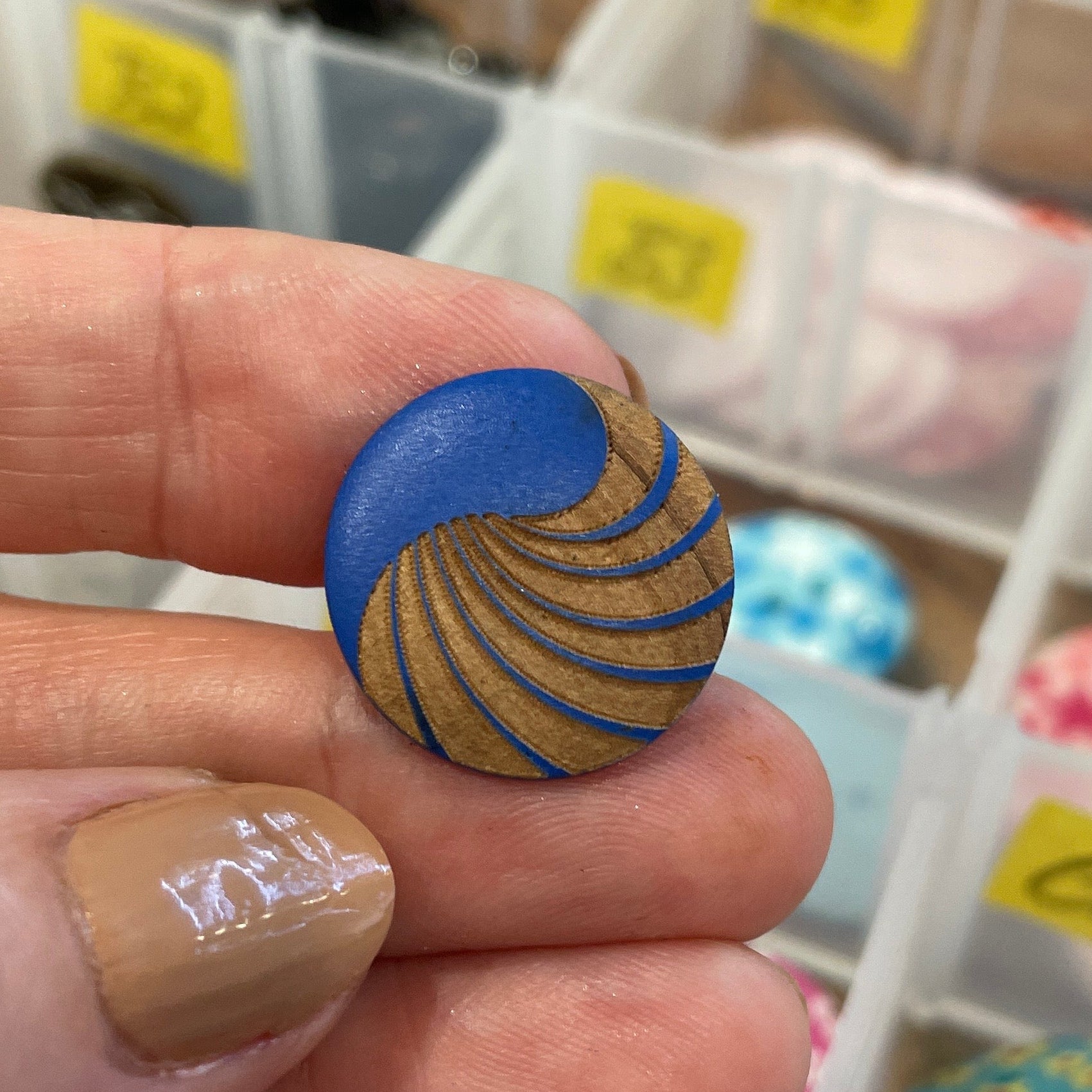 Hand holding a blue and gold textured object with a container of colorful buttons in the background