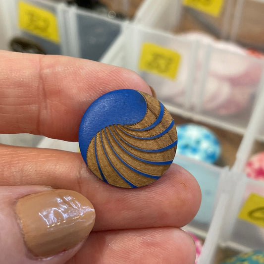 Hand holding a blue and gold textured object with a container of colorful buttons in the background