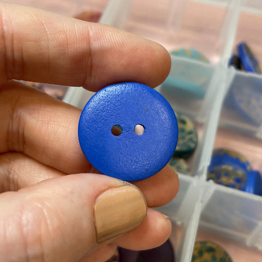 Hand holding a blue button with a container of buttons in the background