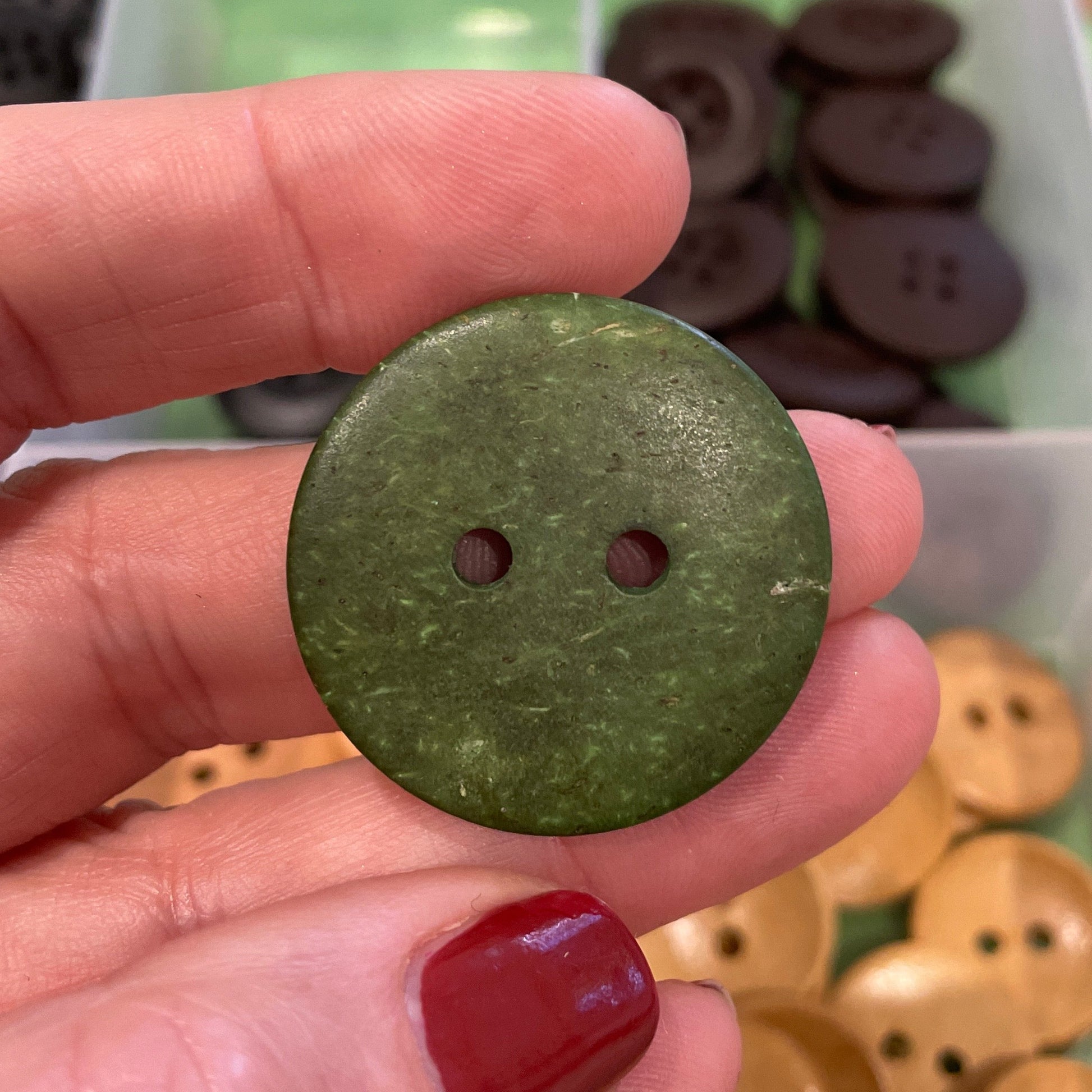 Hand holding a green button with a blurred container of buttons in the background