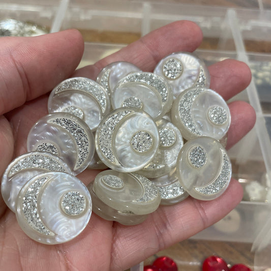 Hand holding decorative buttons with a clear container of more buttons in the background.
