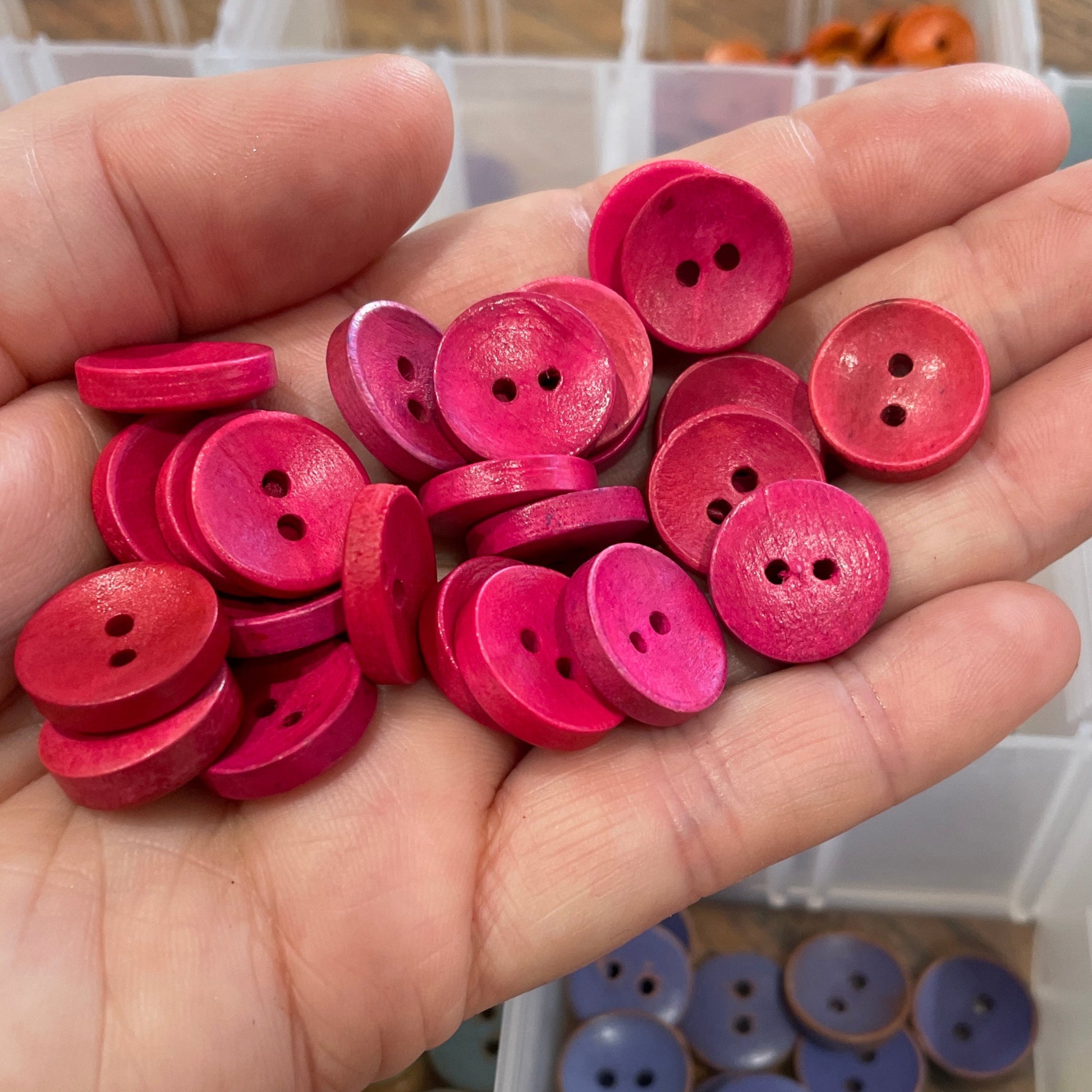 Hand holding pink buttons with a container of assorted buttons in the background.