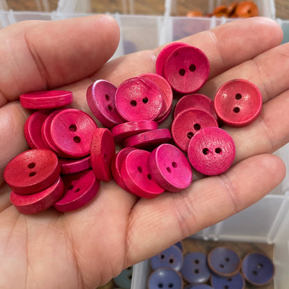 Hand holding pink buttons with a container of assorted buttons in the background.
