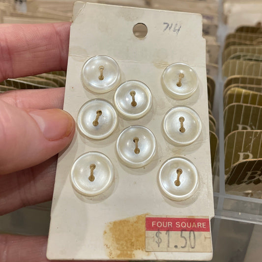 Hand holding a card with white buttons against a blurred background of storage containers.