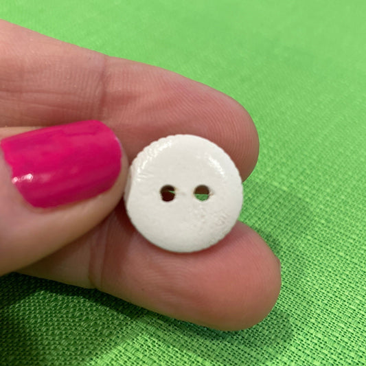 White button held between fingers against a green fabric background