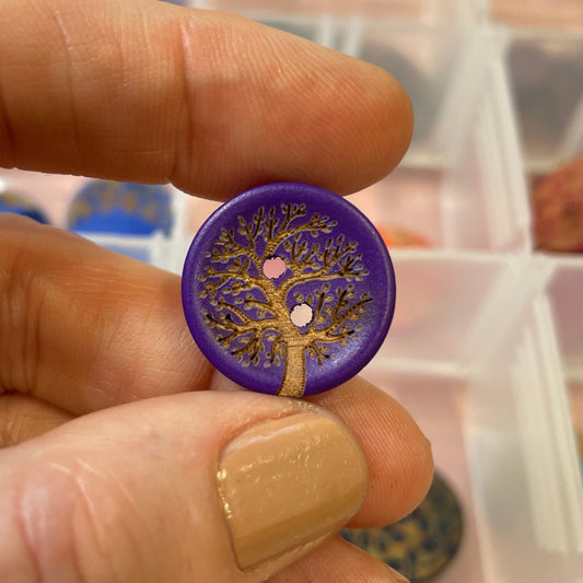 Hand holding a purple button with a tree design against a background of other buttons.
