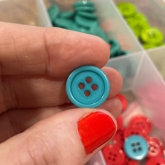 Hand holding a blue button with a container of buttons in the background