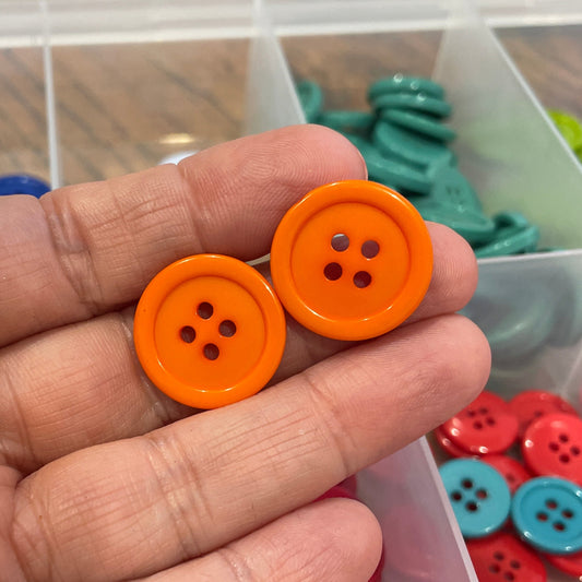 Hand holding two orange buttons with a container of colorful buttons in the background