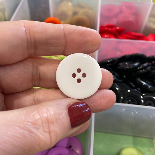 Hand holding a white button with a button collection in the background