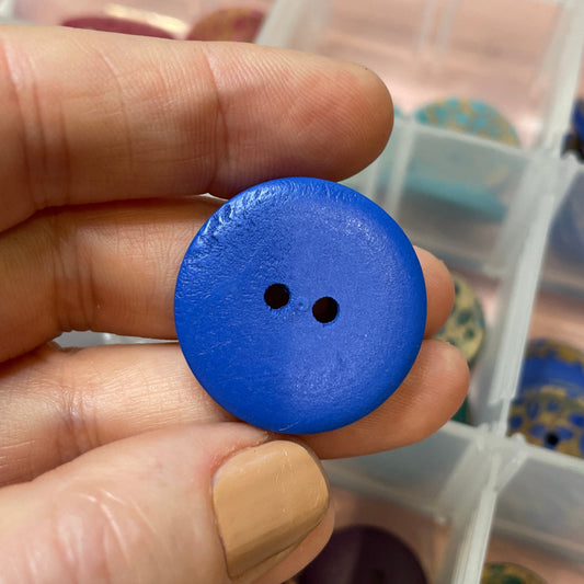 Blue button held by a hand with a container of buttons in the background