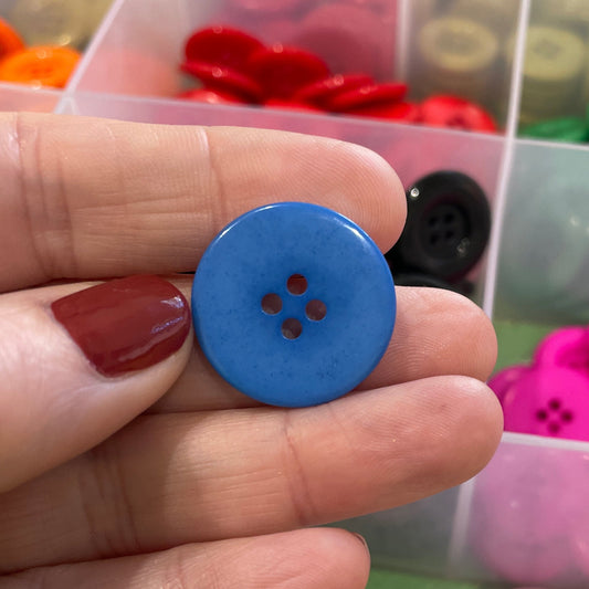 Hand holding a blue button with a container of colorful buttons in the background