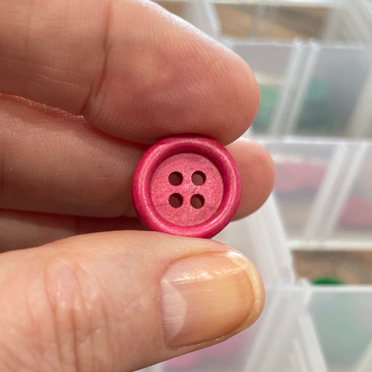 Hand holding a pink button with a container of buttons in the background