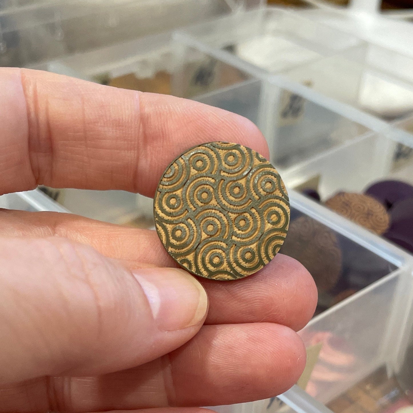 Hand holding a button with a clear container of various items in the background