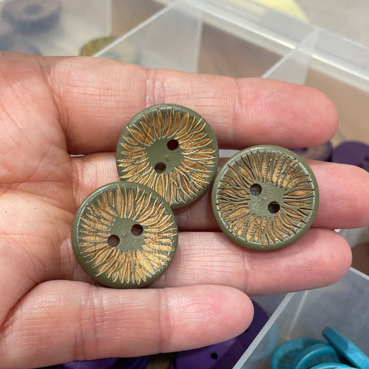 Hand holding three green buttons with a container of assorted buttons in the background