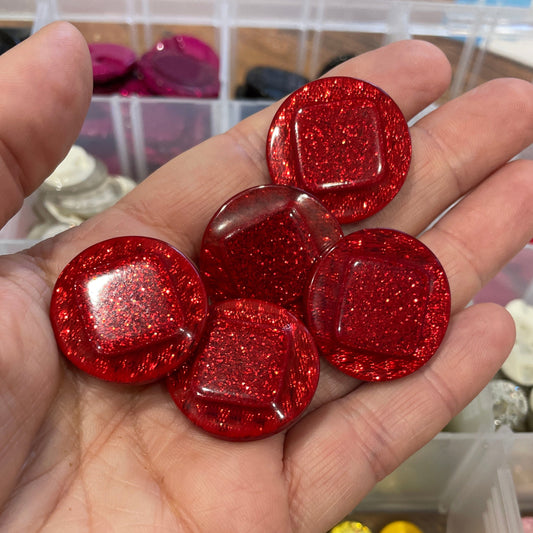 Hand holding red glittery buttons with containers of other buttons in the background
