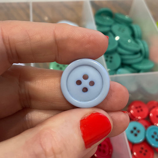 Hand holding a white button with a container of colorful buttons in the background