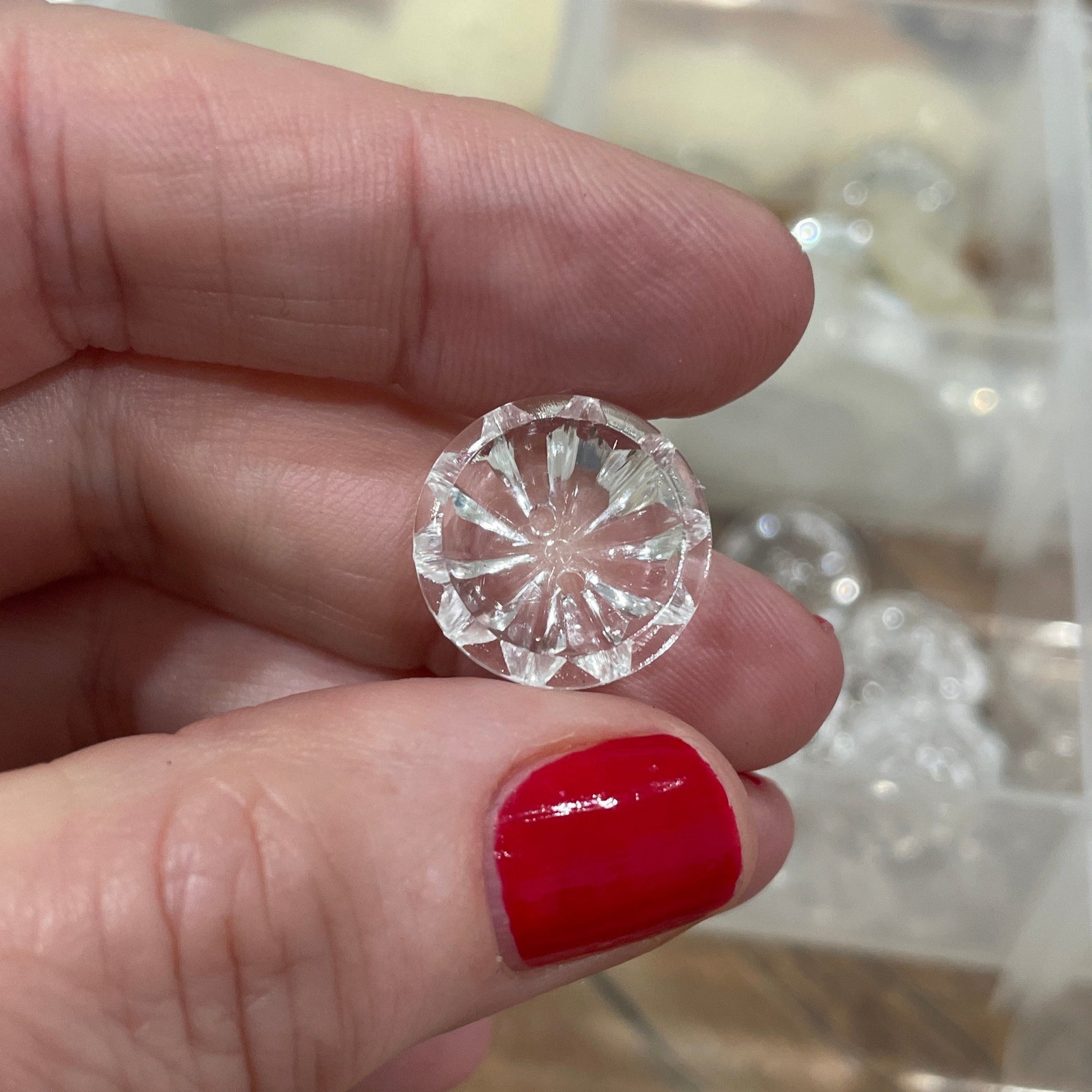 Hand holding a clear gemstone with a blurred background of jewelry display