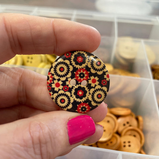 Hand holding a decorative button with floral pattern in front of a container of cookies.