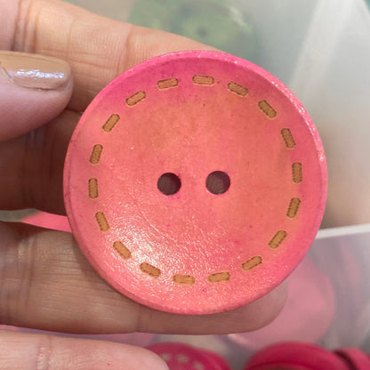 Pink button held by a hand with more buttons in the background