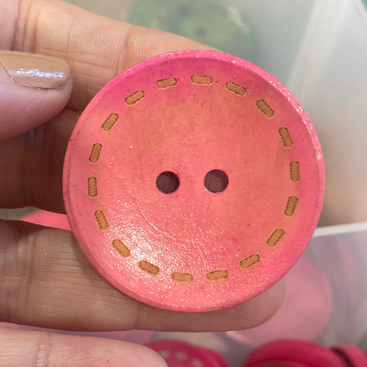 Pink button held by a hand with more buttons in the background