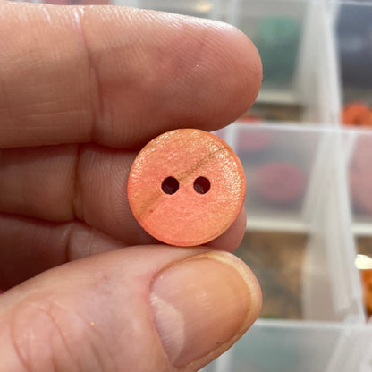 Hand holding a small pink button with a blurred background of a button collection.