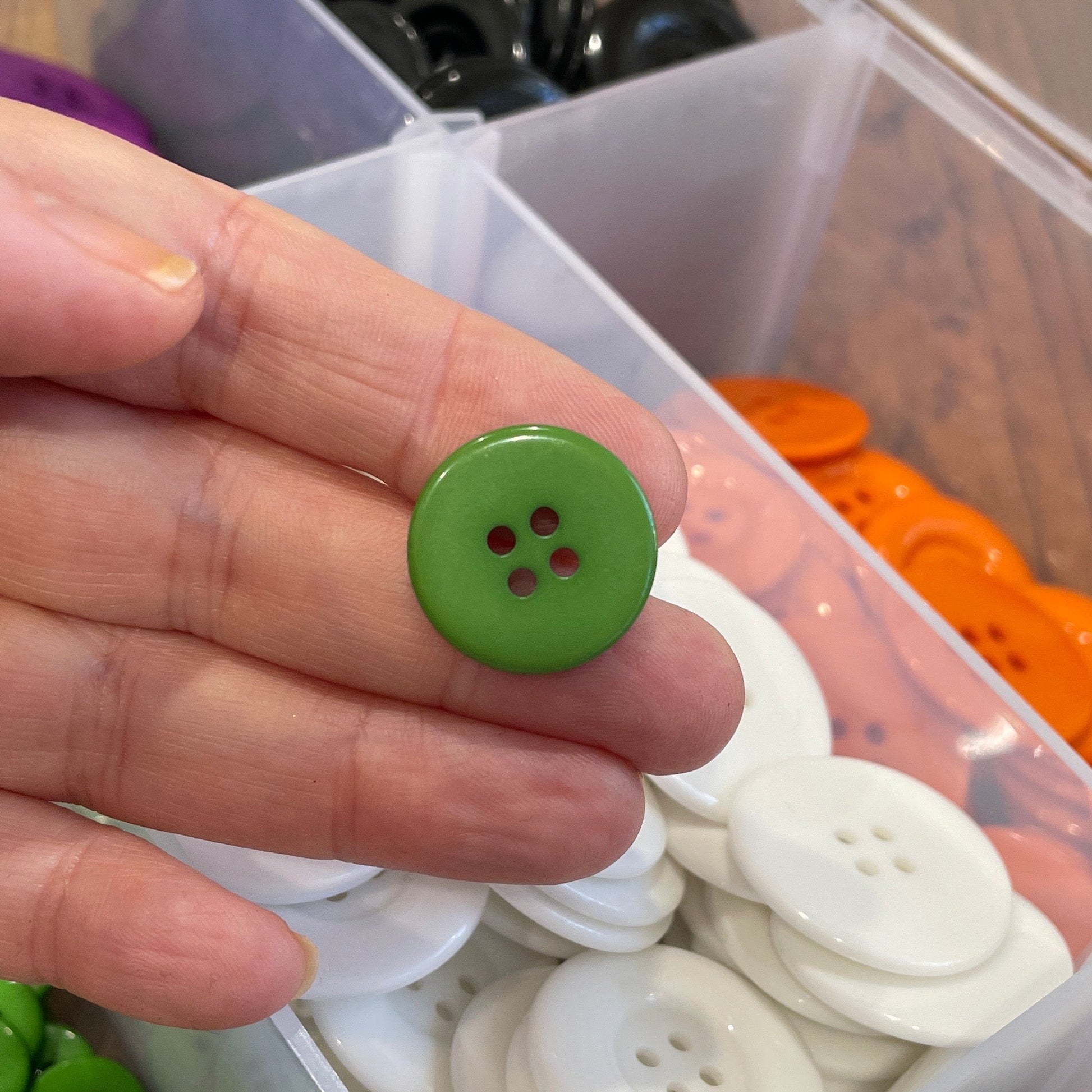 Hand holding a green button with a container of buttons in the background