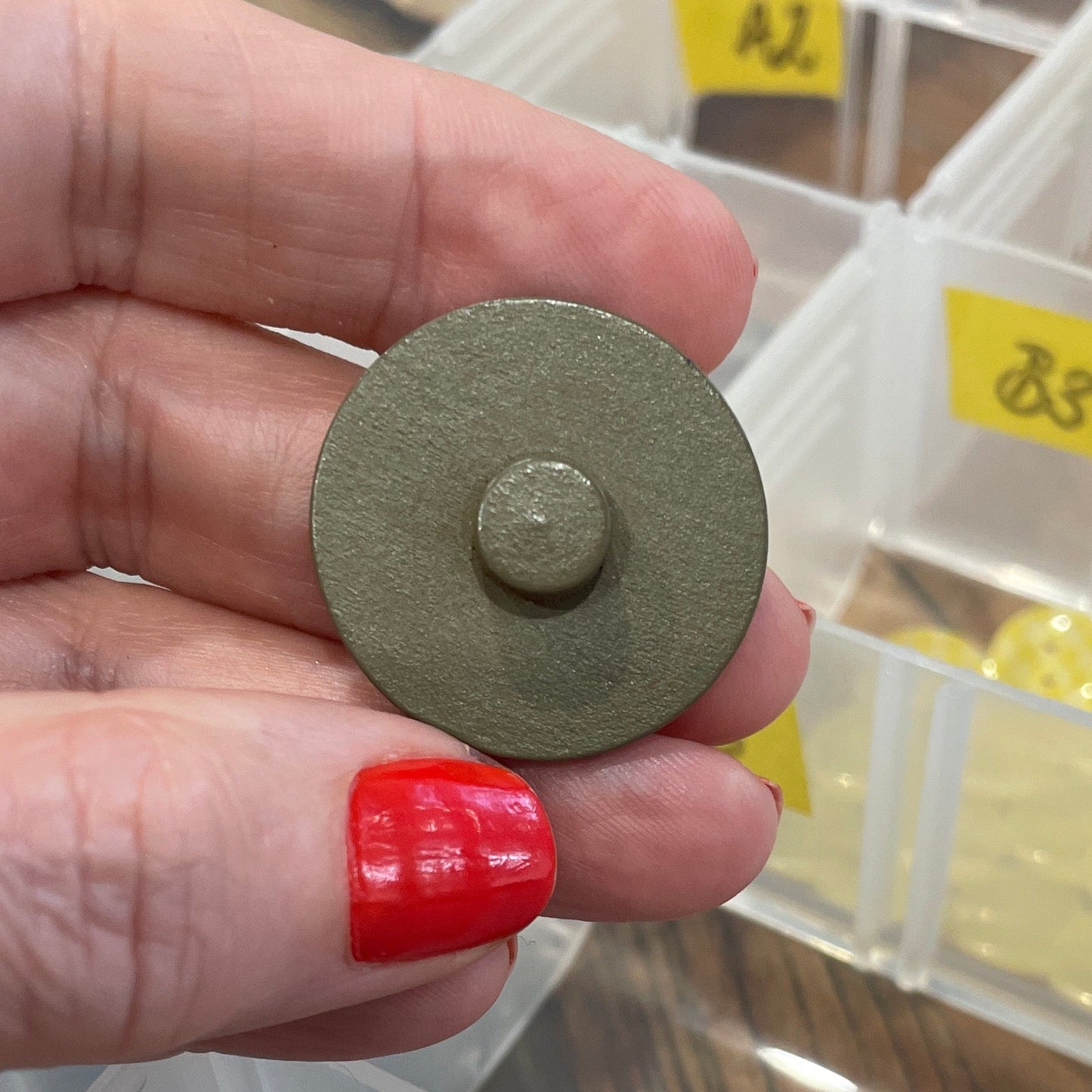 Hand holding a button with a blurred background of button storage containers.