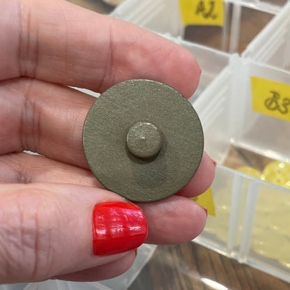 Hand holding a button with a blurred background of button storage containers.