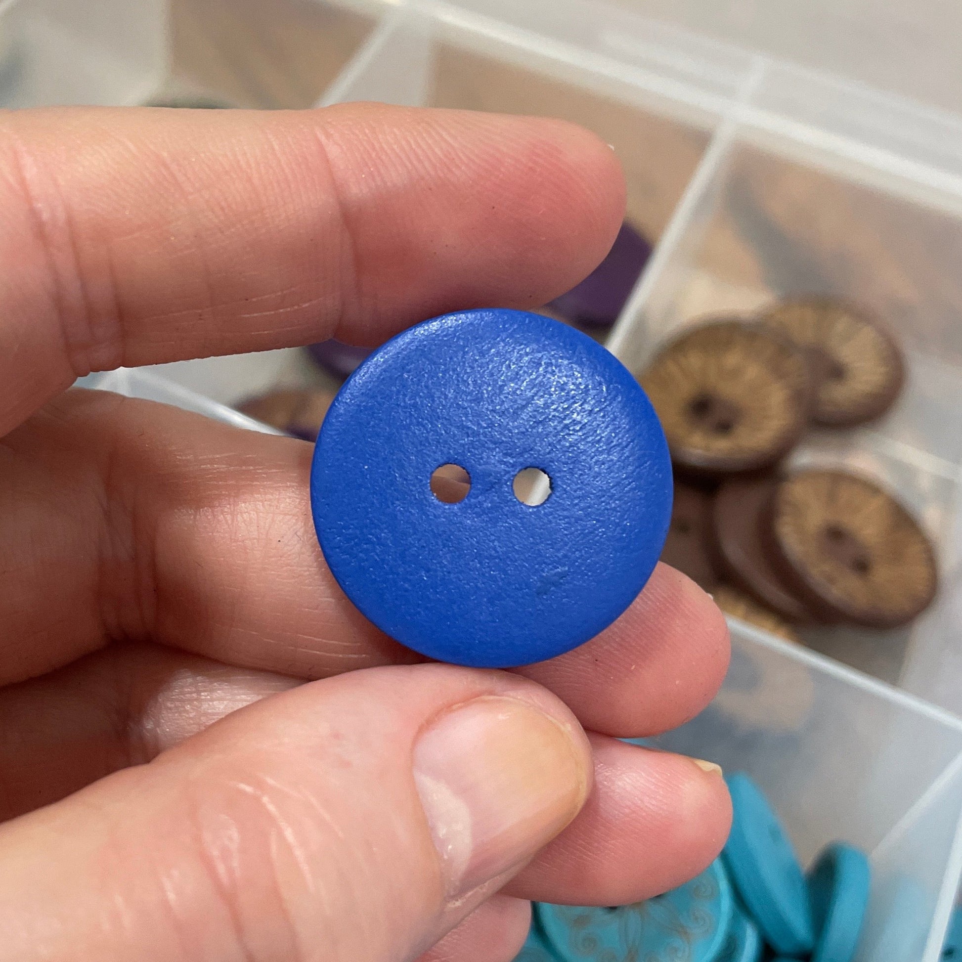Hand holding a blue button with a container of buttons in the background