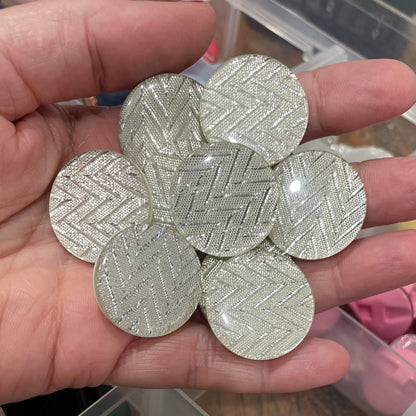 Hand holding silver hexagonal buttons with a container of various colored buttons in the background.