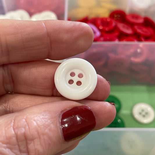 Hand holding a white button with a colorful button collection in the background