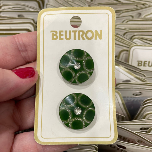 Green patterned buttons on a Beutron card held by a hand with red nail polish.