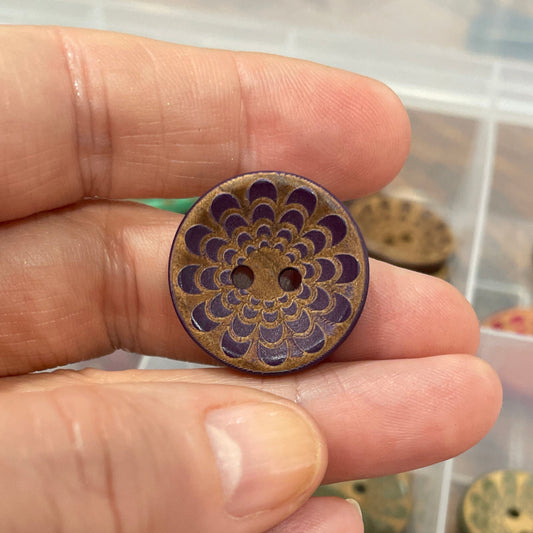 Hand holding a decorative button with a container of similar buttons in the background