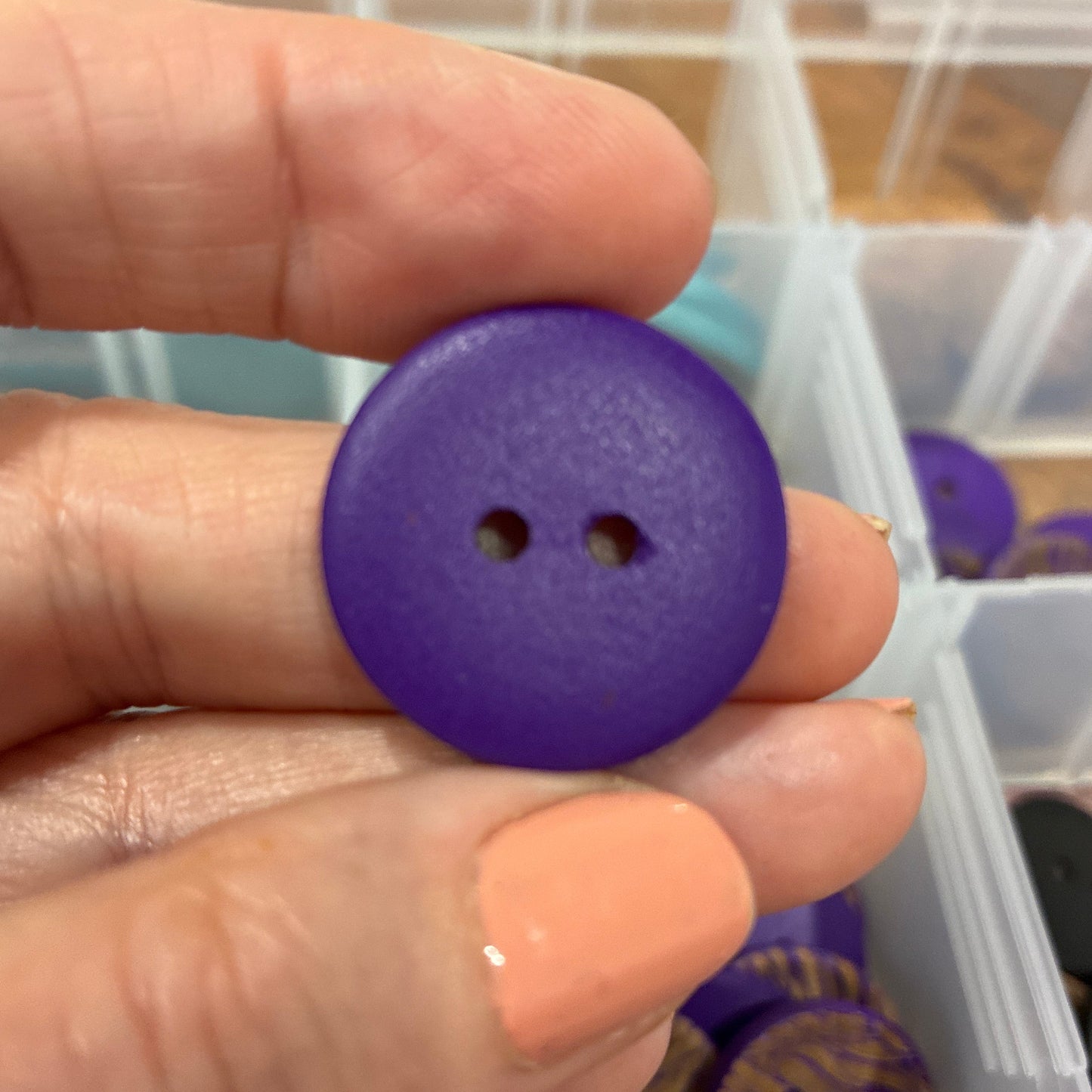 Hand holding a purple button with a container of buttons in the background