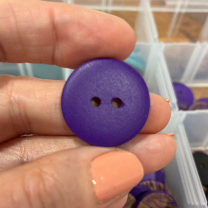 Hand holding a purple button with a container of buttons in the background