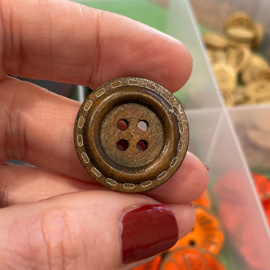 Hand holding a gold button with a container of colorful buttons in the background