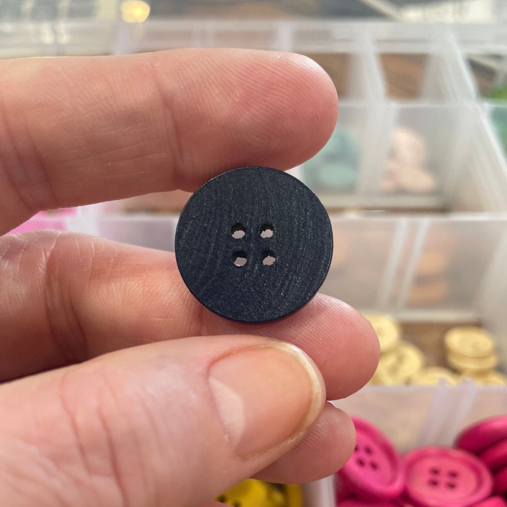 Black button held between fingers with a container of colorful buttons in the background