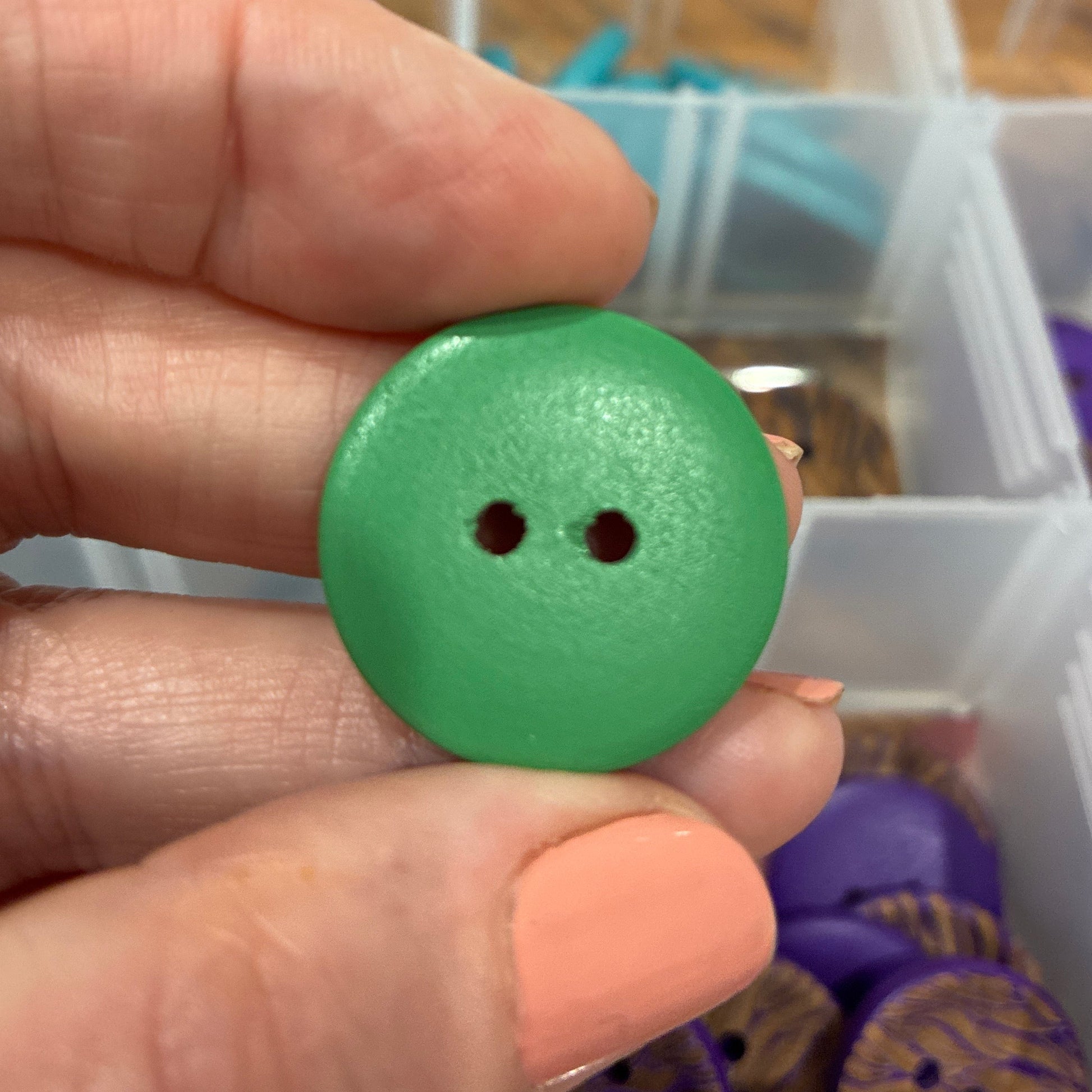 Green button held between fingers with a blurred background