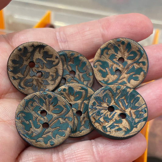 Hand holding decorative buttons with a blurred background of more buttons and a container.