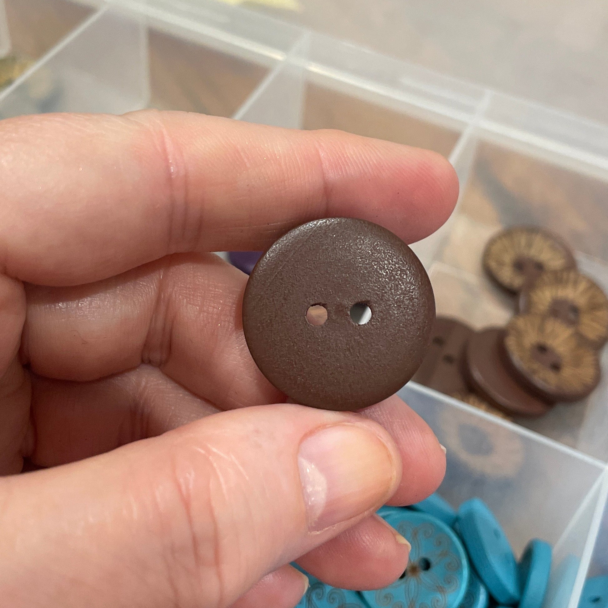 Hand holding a brown button with a container of blue buttons in the background